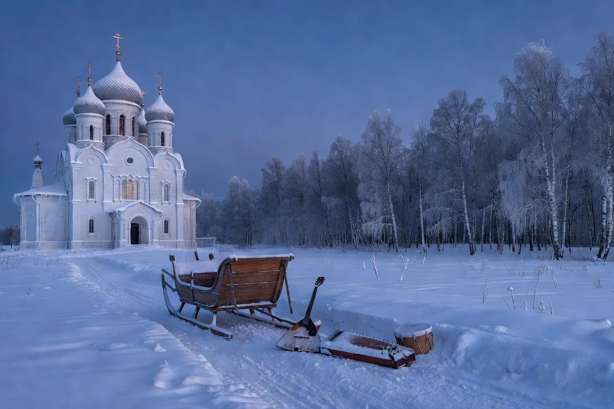 Paysage d'hiver russe au crépuscule, église enneigée aux coupoles, traîneau et instruments traditionnels sur un chemin blanc